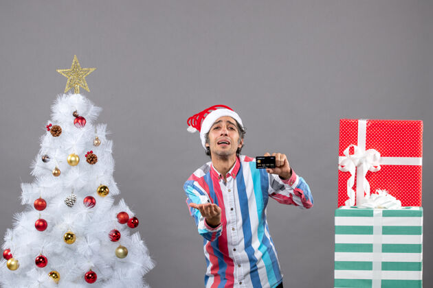 圣诞前视图绝望的男子信用卡站在白色圣诞树附近快乐微笑灰色