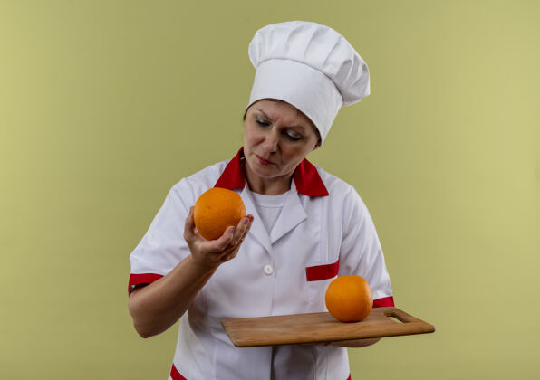 手持想着穿着厨师制服的中年女厨师 手里拿着橘子放在砧板上 看着橘子手板子中年