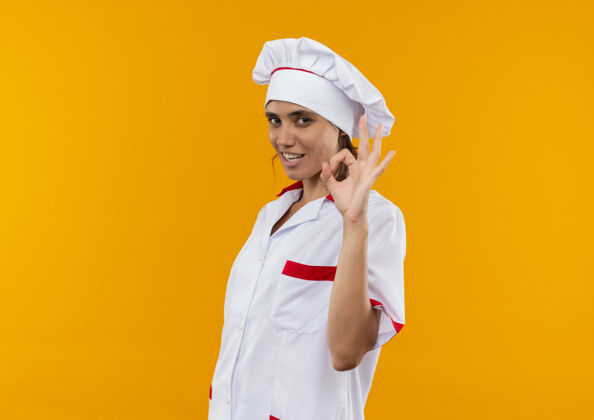 好的微笑着的年轻女厨师穿着厨师制服 展示着模仿空间的奥基手势厨师穿着手势