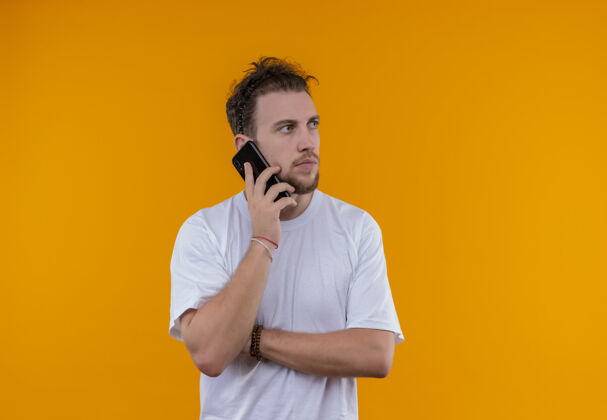 年轻看着身边穿着白色t恤的年轻人在电话里说话 在孤立的橙色背景下交叉手白色男人说话