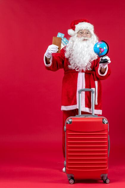 人圣诞老人的前视图 带着包 拿着票 准备在红墙上旅行前面举行服装