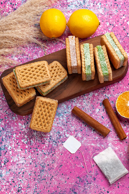 柠檬顶视图美味的三明治饼干与柠檬和肉桂在粉红色的办公桌上糖果饼干顶部