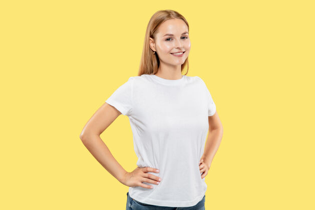 成功黄色工作室背景上的白人年轻女子半身像穿着白衬衫的漂亮女模特人类情感的概念 面部表情微笑 双手放在臀部站立手势表情肖像