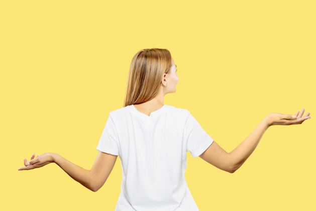 员工黄色工作室背景上的白人年轻女子半身像穿着白衬衫的漂亮女模特人类情感的概念 面部表情展示一个空的空间或邀请女性手势金发