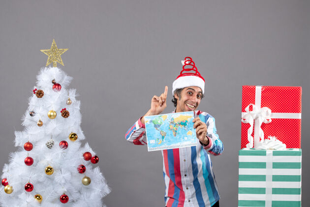 举行正面图快乐男子戴着螺旋弹簧圣诞帽望着高高举着世界地图指着高高圣诞老人家伙地图