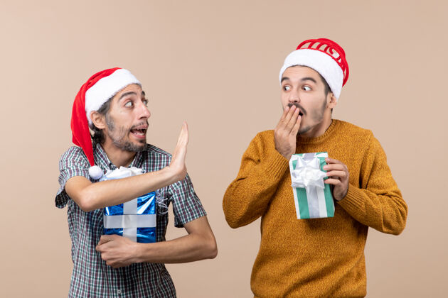 持有前视图两个困惑的家伙分享秘密 并持有在米色孤立的背景圣诞礼物成人分享礼物
