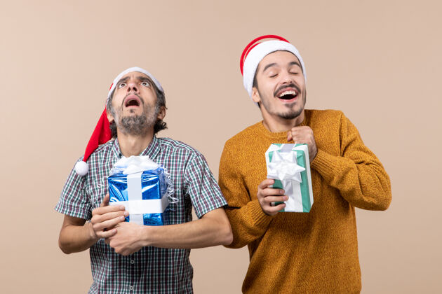 两个正面图两个男人一惊一喜地拿着米色背景的圣诞礼物两个伙计们男人欢快