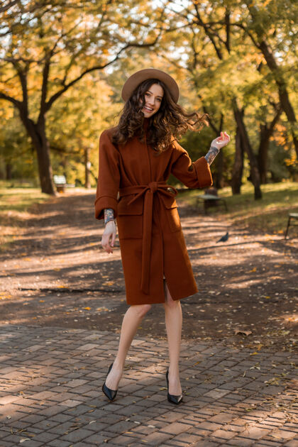 阳光迷人时尚微笑的瘦身女子卷发漫步公园身着暖棕色外套 秋日时尚街头风女士户外夹克