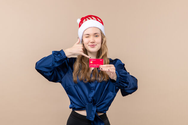 圣诞节正面图年轻女性手持红色银行卡在粉色背景上过节照片新年钱情孩子天真年轻的女性