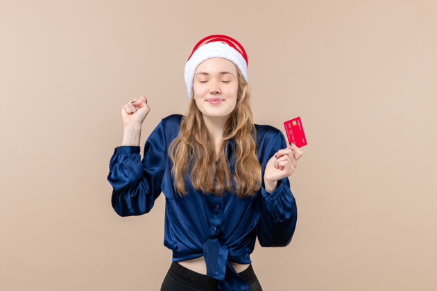 钱正面图年轻女性手持粉色背景的红色银行卡圣诞钱照片节日新年情绪女举行圣诞节