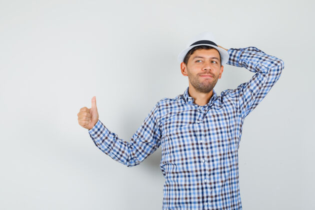 表情穿着格子衬衫的年轻男子手放在帽子上竖起大拇指 看上去很满意虚拟站立男人