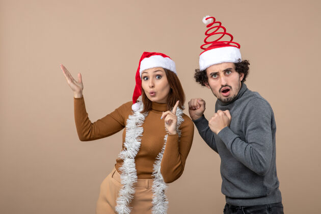 情侣圣诞节心情激动凉爽满意惊喜可爱情侣戴着红色圣诞老人帽指着上方帽子成人人们