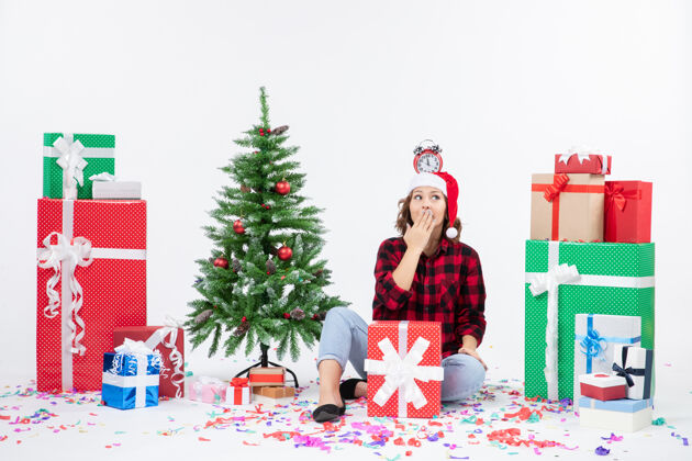 冬青一位年轻女子坐在一堵白墙上 头上拿着钟 围着礼物转节日快乐装饰