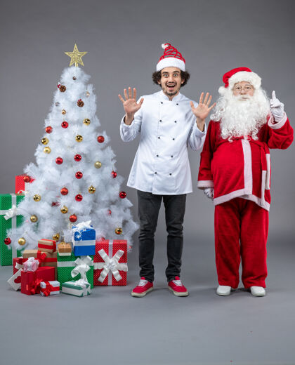 孩子圣诞老人和男厨师在灰色墙上围着圣诞礼物的正视图圣诞老人前面圣诞老人