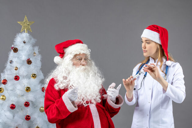 医生圣诞老人和女医生在灰色墙上打针的前视图快乐十二月女性