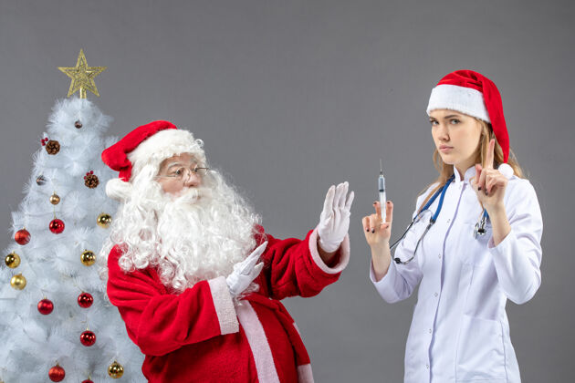 圣诞节圣诞老人和女医生在灰色墙壁上准备注射的正视图正面圣诞老人快乐