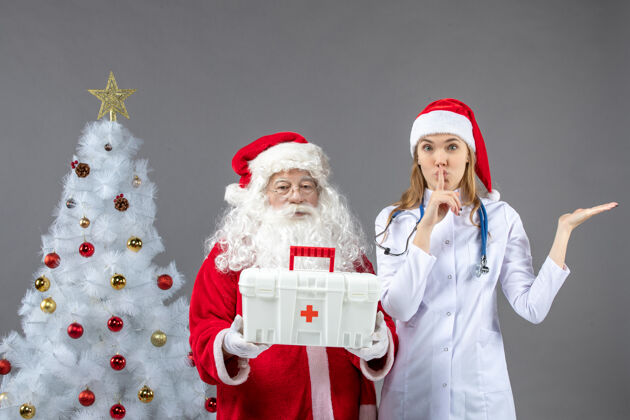 护士圣诞老人和给他急救箱的女医生在灰色墙上的正视图快乐实验室庆祝