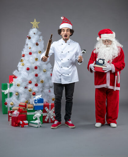 圣诞快乐圣诞老人和男厨师在灰色墙上围着圣诞礼物的正视图雪快乐圣诞老人