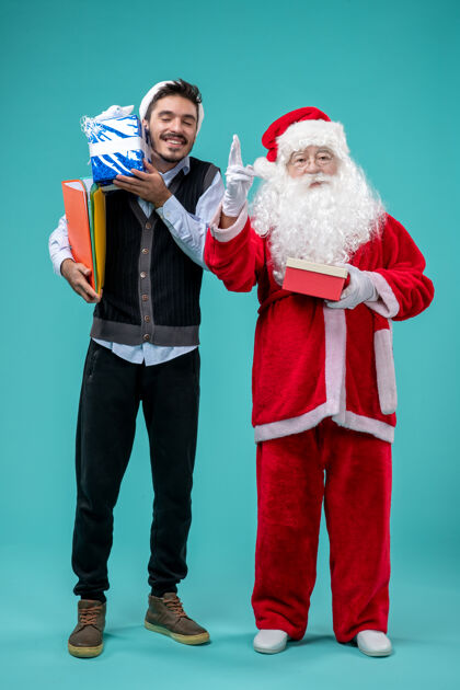 微笑前视图圣诞老人与年轻的男性和礼物上的蓝色背景前面蓝色男人