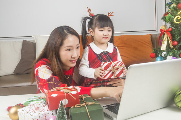 圣诞节快乐的妈妈和小女儿在家装饰圣诞树和礼物中国人女孩人
