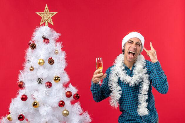 装饰圣诞节心情与情绪激动的年轻人圣诞老人帽子在一个蓝色条纹衬衫举行了一个靠近圣诞树的葡萄酒杯夏娃年轻人心情