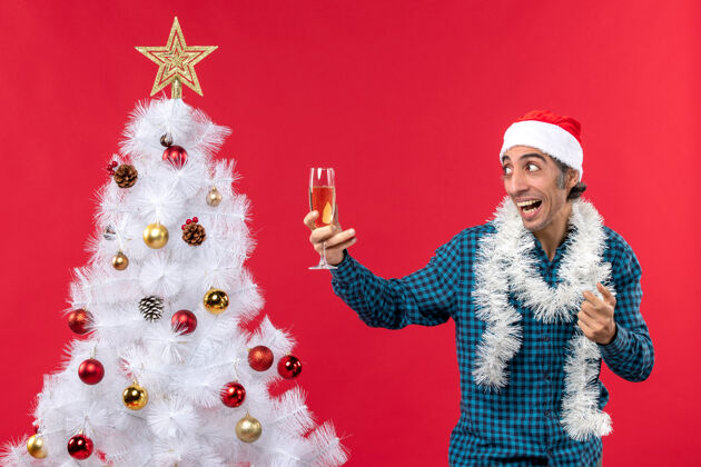 葡萄酒圣诞节心情与情绪激动的年轻人圣诞老人帽子在一个蓝色条纹衬衫举行了一杯葡萄酒摆在圣诞树附近心情人装饰