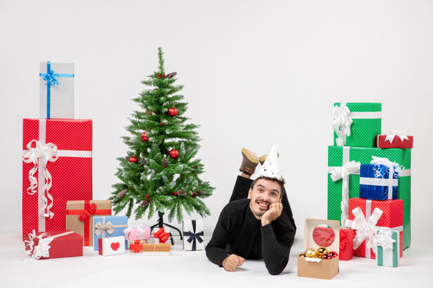 礼物年轻人躺在白色墙上微笑的节日礼物周围的正面视图冬青礼物礼物