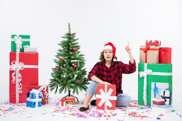 节日年轻女子围坐在圣诞礼物和白色墙上的小圣诞树前的视图礼物庆祝快乐