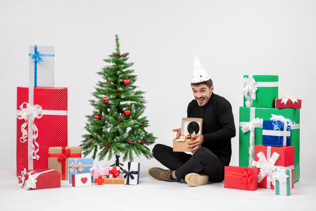 模型年轻人坐在白色墙上的节日礼物周围的正面视图盒子礼物季节