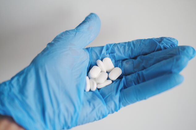 卫生学一个人戴着蓝色手套拿着白色药片的手的特写镜头大流行治疗疾病