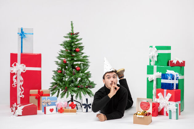节日年轻人躺在白色墙上的节日礼物周围的正面视图人礼物树