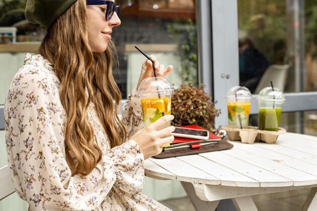 美味中镜头的年轻女子拿着新鲜的饮料坐在桌边异国情调健康水果