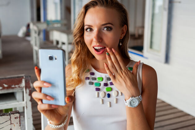 女人一位身着白色礼服的美女戴着墨镜在夏日咖啡馆用手机拍照电话手机时尚