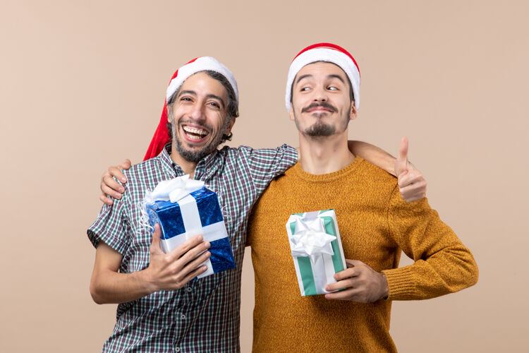 米色前视图两个微笑的家伙拥抱和举行在米色孤立的背景圣诞礼物礼物拥抱圣诞节