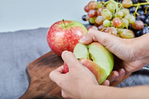 手把一个苹果切成两半 把一束葡萄放在木板上高质量的照片收获切割桌子