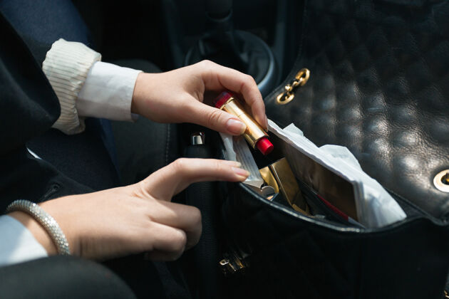 检查年轻女人坐在车里 拿着口红从手提包里出来口红搜索包