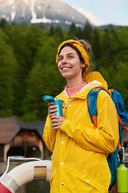 森林垂直拍摄的快乐年轻的欧洲女性穿着黄色的帆布背包 摆在木筏船对落基山脉和森林水体贴人