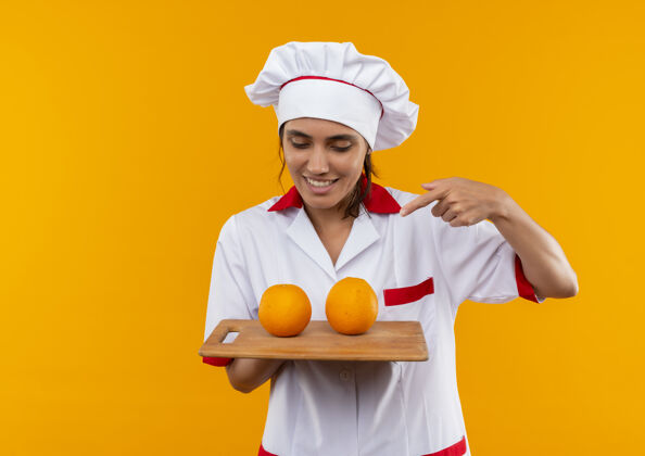 穿年轻的女厨师面带微笑 穿着厨师制服 手拿着橘黄色的裁板 在裁板上留有复印空间板子切分