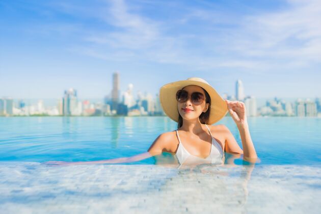 著名肖像美丽的亚洲年轻女子微笑放松休闲围绕室外游泳池与城市景观现代外部亚洲