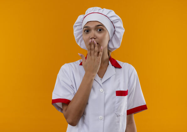 制服惊讶的年轻厨师女身穿厨师制服捂着嘴 手放在孤立的橙色背景上 留有复印空间穿着女封面