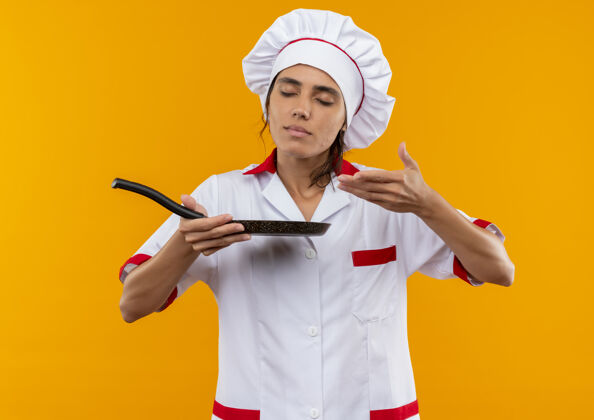 厨师年轻的女厨师闭着眼睛 穿着厨师制服 手持并假装闻到了煎锅的味道制服厨师封闭