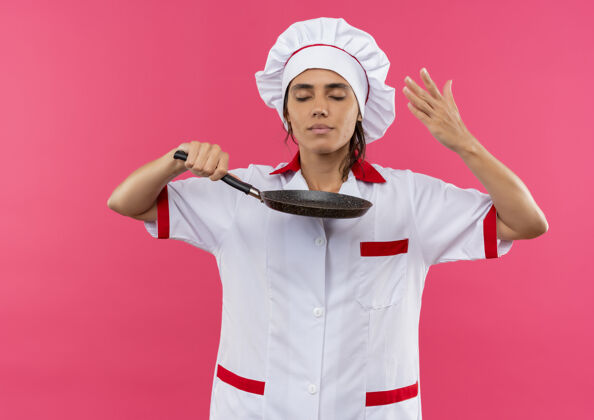 平底锅年轻的女厨师闭着眼睛 穿着厨师制服 拿着一个有复印空间的煎锅 嗅着味道闻着封闭厨师