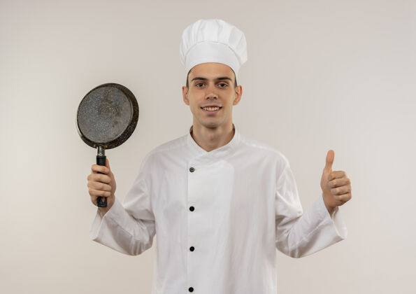 厨师面带微笑的年轻男厨师穿着厨师制服 举着煎锅 拇指朝上穿制服向上