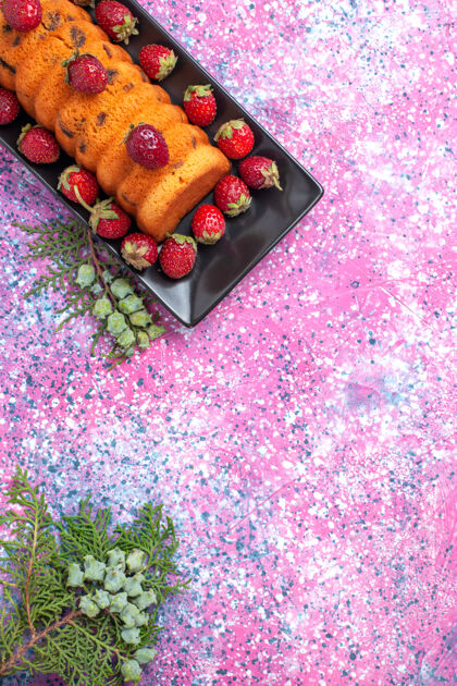 草莓顶视图美味的蛋糕在黑色的蛋糕锅里 粉红色的桌子上放着新鲜的红色草莓红色鲜花糖