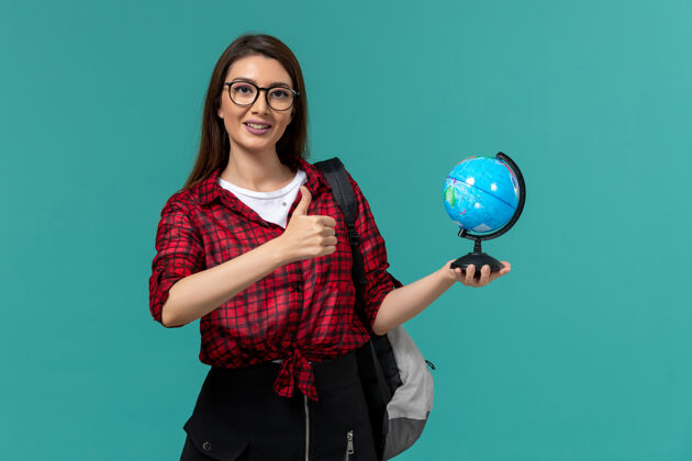 人女学生背着背包 手持浅蓝色墙上的小地球仪的正面图保持课大学