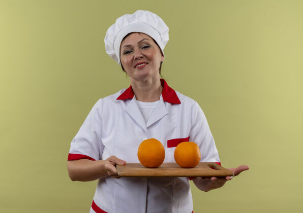 持有微笑的中年女厨师身着厨师制服 拿着橘子放在有复印空间的砧板上中年女董事会
