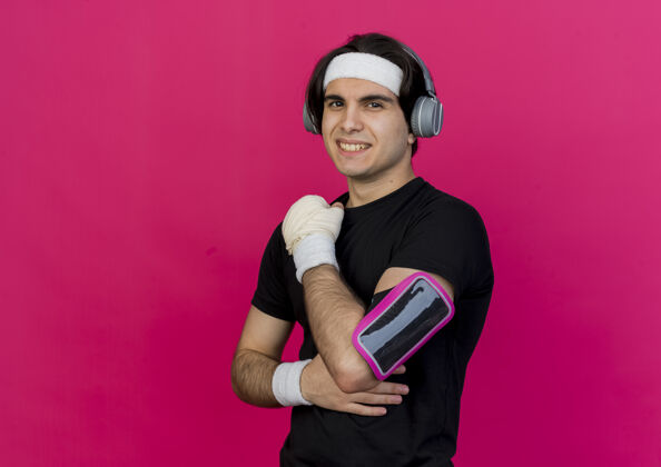 快乐年轻的运动型男士 穿着运动服 头戴健康手机和智能手机袖标 微笑自信 快乐 积极粉色自信运动装