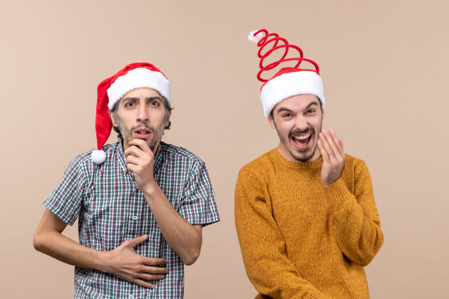圣诞节前视图两个圣诞节的家伙一个困惑和一个快乐的圣诞老人帽子米色孤立的背景男帽子两个圣诞老人