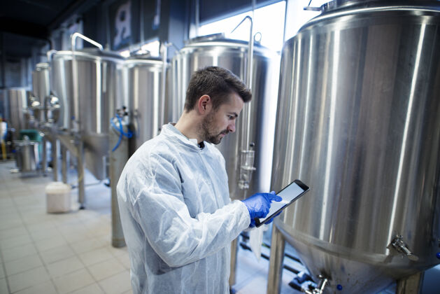 白色套装技术专家站在食品生产厂的平板电脑上打字集中轨道金发