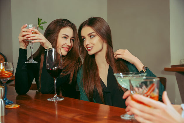 漂亮女朋友在酒吧喝酒她们坐在一张有鸡尾酒的木桌旁酒精团体干燥